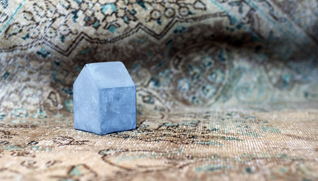 Presse papier maison en béton brut posée sur un tapis beige turquoise